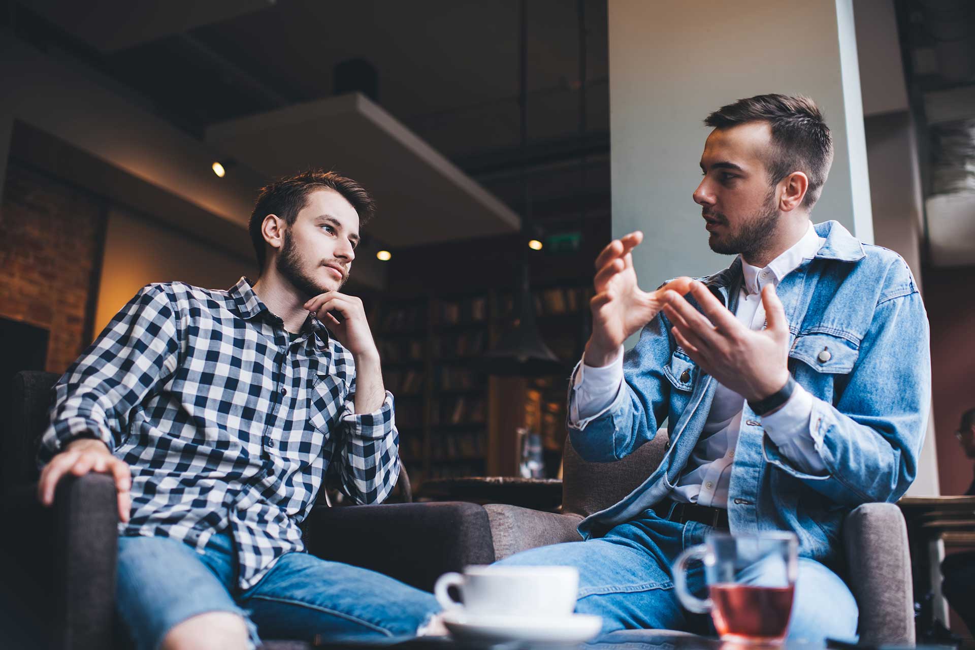 Two young men in conversation over coffee, one gesturing as he talks